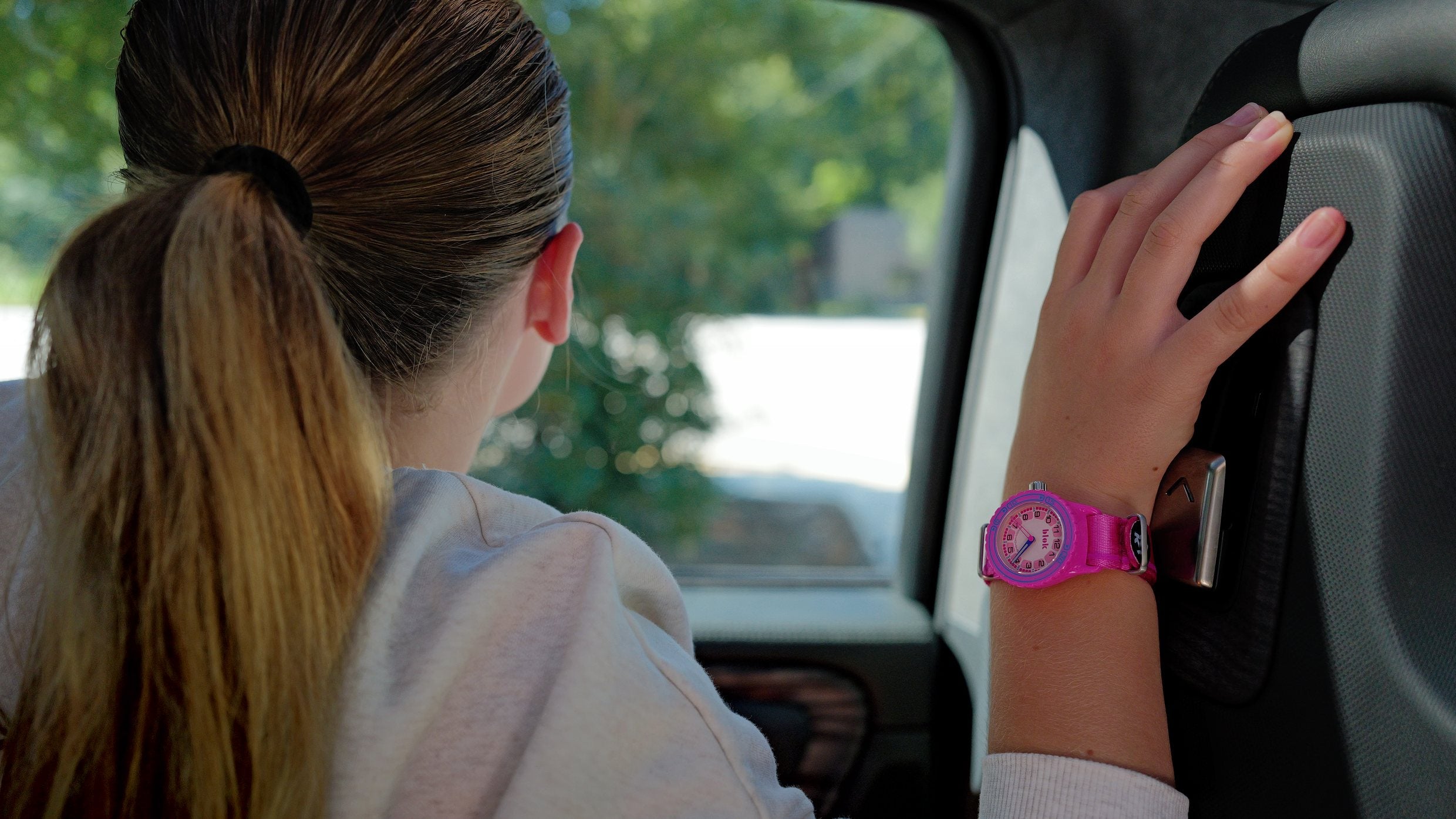 A girl in the back seat of a car, hand on the door, wearing a fuchsia BLOK 33